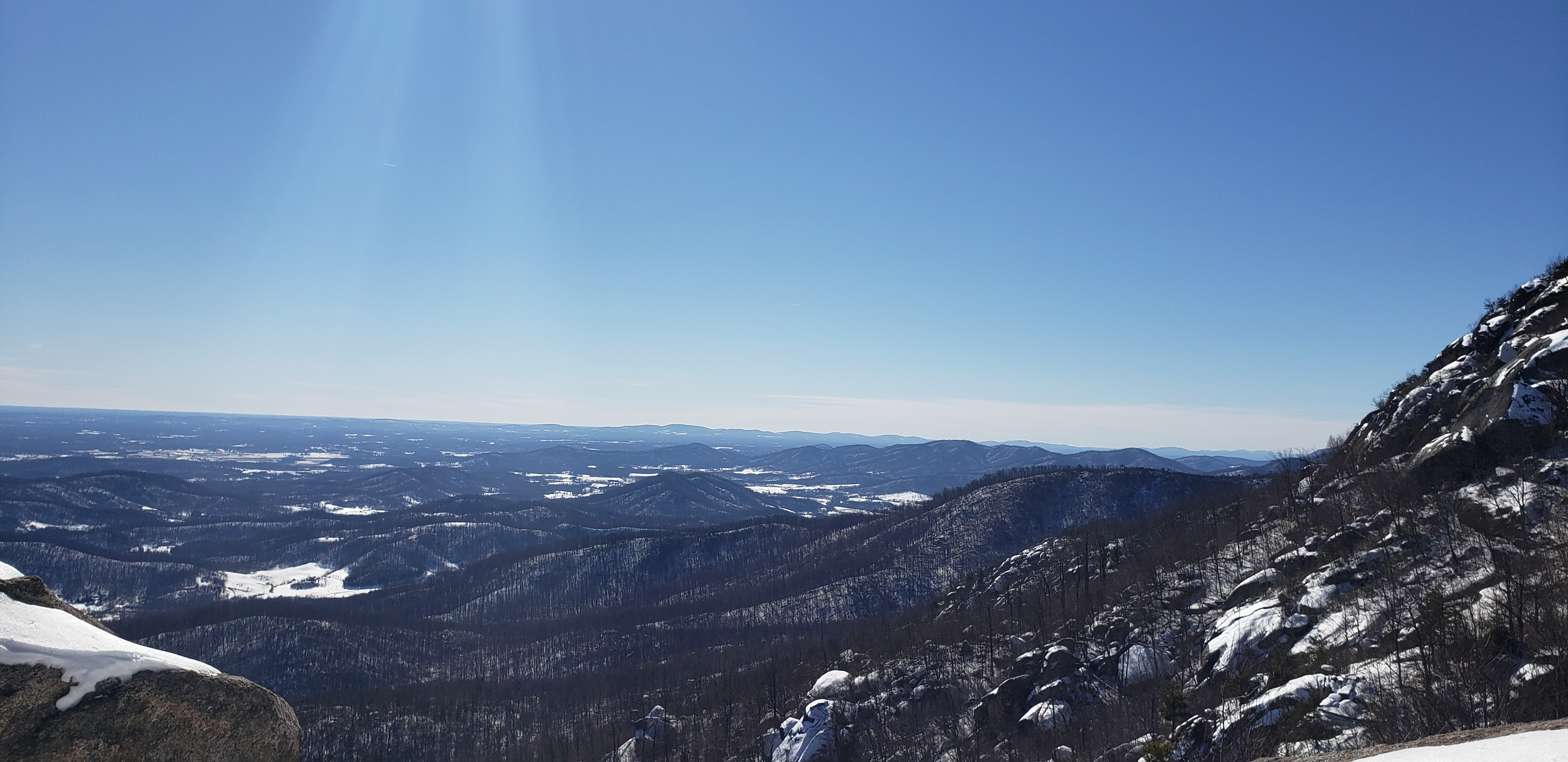 A vast valley of low mountains and farmland under a sunbeam and a clear sky.